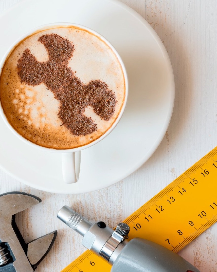 Cappuccino mit Schraubenschlüssel im Milchschaum, daneben Reparatur-Werkzeug